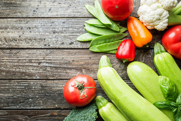 assortment of fresh vegetables cauliflower, broccoli, zucchini and tomatoes on wooden background with space for text
