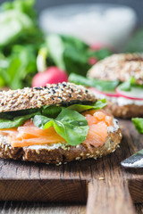 Bagels with cream cheese avocado, fish, arugula and radish on old wooden table. Healthy breakfast food.