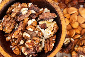 Peeled walnut in a wooden cedar plate on the background a scattering of various nuts. Peeled walnut pattern
