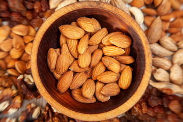 Peeled almonds in a wooden cedar plate on the background a scattering of various nuts. Peeled almonds  pattern