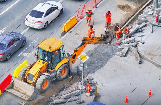 Bulldozer with group of workers wear safety uniform during road works in an asphalt road. New kerb stones on gravel ground placing road edge at construction site. Machine labor builder digging highway