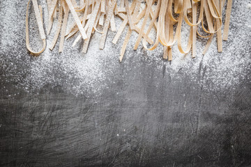 Raw uncooked homemade pasta with flour over dark background. Top view with space for text.