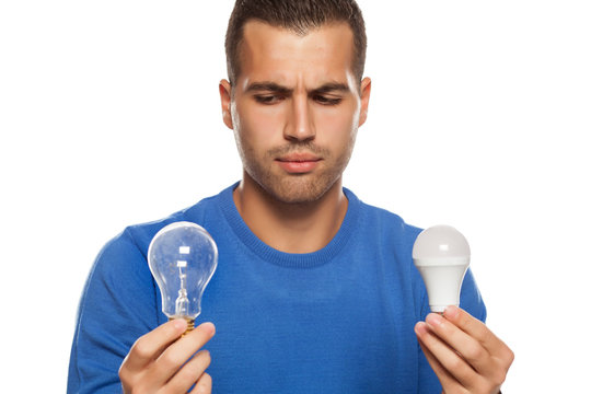 portrait of young man, holding LED bulb and old fachion bulb on white background