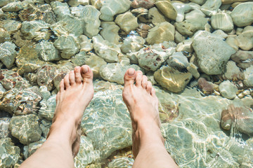 Female legs near clean sea with stone. Summer vacation. Close up. Girl at the resort.