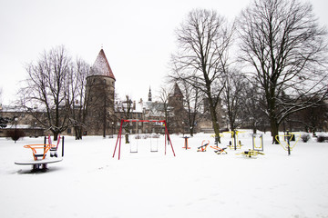 Naklejka premium towers and medieval walls of the city of Tallinn in Estonia, with a playground for children in the middle of frozen snow. Life in winter in the Baltic countries, in Estonia