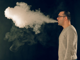smoking man in e-cigarette smoke on black background