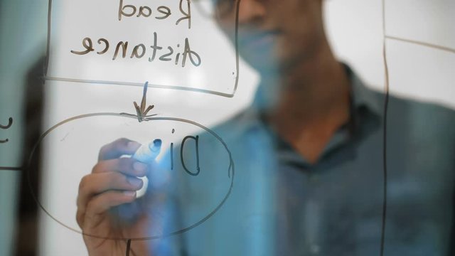 Close up of Indian man drawing part of chart on glass board with black marker