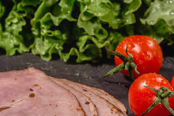 Ingredients for cooking Italian bruschetta on dark table. Italian bruschetta with cherry tomatoes, cheese sauce, salad leaves, garlic, olive oil and ham
