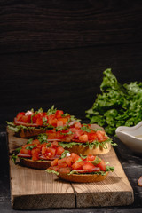 Tasty savory tomato Italian appetizers, or bruschetta, on slices of toasted baguette garnished with salad leaves, ham, chopped tomato and sauce, close up on a wooden board