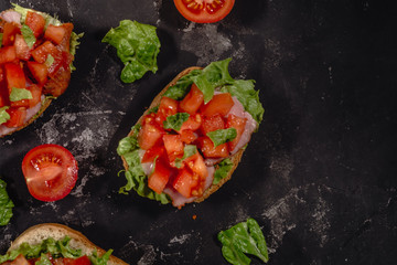 Traditional Italian Bruschetta with tomatoes, sauce, salad leaves and ham on a dark baton background. Traditional Italian appetizer or snack, antipasto. Top view with copy space, copy-paste. Flat lay