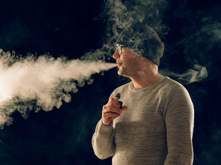 smoking man in e-cigarette smoke on black background
