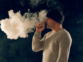 smoking man in e-cigarette smoke on black background