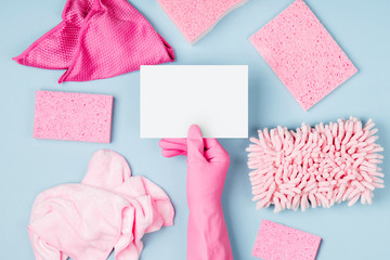 Female hands hold empty card. Blue background with Detergents and cleaning accessories  in pink...