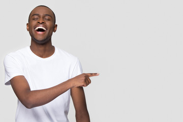 Happy african man laughing out loud at funny joke pointing finger aside at copy space, jovial...
