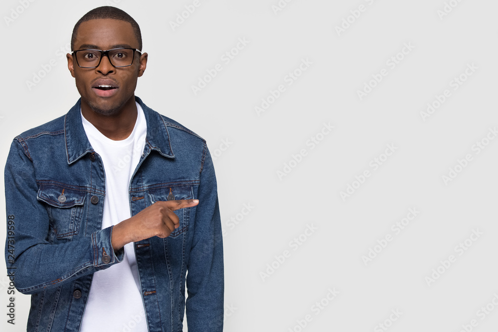 Wall mural Shocked african man student pointing finger aside at copy space surprised astonished looking at camera isolated on white grey studio background, stunned black guy advertise unbelievable presentation