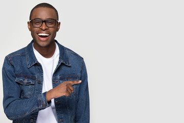 Happy excited african man customer laughing pointing finger aside at copy space, cheerful black guy advertising fun optics denim shop or dental service sale offer isolated on white studio background