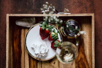 Strawberries with cream and glass of white wine on wooden tray