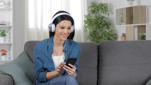 Lady searching and listening to music on smart phone sitting on a couch at home