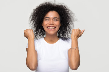 Excited happy young african american woman feeling overjoyed isolated at white grey studio background, lucky euphoric black girl winner celebrating win victory success raising hands in yes gesture