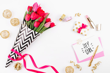 Pink and Gold Styled Desk with Florals. Pink tulips in black and white stylish wrapping paper, gifts, cosmetics and female accessories with confetti on white background