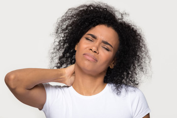 Tired upset african young woman massaging hurt stiff neck isolated on white grey studio background, fatigued sad black lady rubbing tensed muscles to relieve joint shoulder pain, fibromyalgia concept