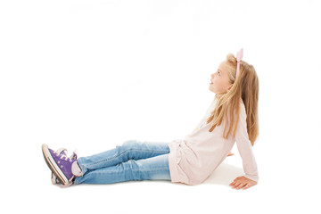 Beautiful little girl sitting on floor, looking on copy space. Isolated on white background