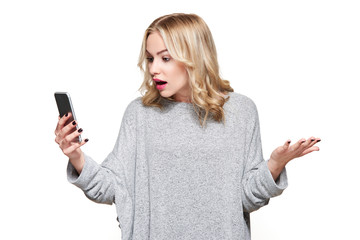 Shocked angry young woman looking at her mobile phone in disbelief. Woman staring at shocking text message on her phone, isolated over white background.