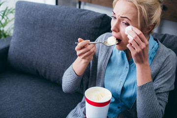 woman eating ice cream and crying while siitng on couch at home alone