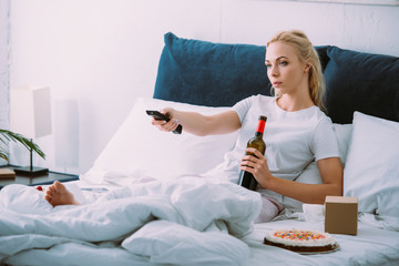 sad woman with wine bottle watching tv while celebrating birthday in bed alone