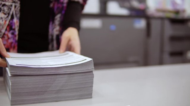 female worker brings printed brochures corrects a stack of papers