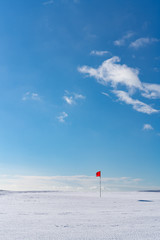 Snow covered deserted golf green with red flag, on Cleeve Hill, Cotswolds, Gloucester UK