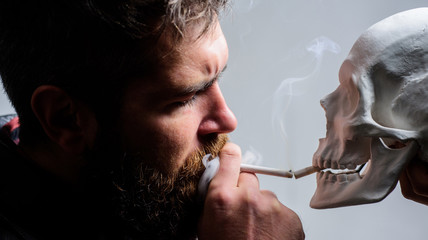 Fototapeta premium Harmful habits. Destroy your health. Smoking is harmful. Habit to smoke tobacco bring harm to your body. Smoking cause health damage and death. Man smoking cigarette near human skull symbol of death