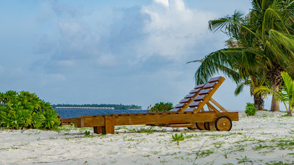 Strandliege aus Holz unter Palmen am Strand auf Insel  Adaaran Select Meedhupparu auf Malediven im Indischen Ozean
