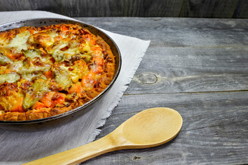 Pie with vegetables and cheese in a vintage pan with a wooden spoon on a white linen napkin on wooden rustic background