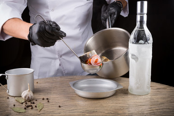 Cook in black gloves is serving fish soup