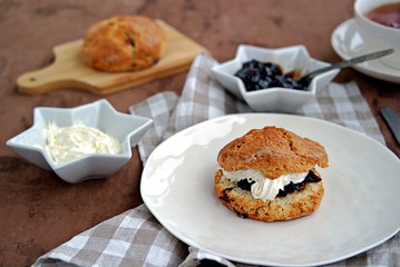 Traditional English scones with dried cranberries on a white plate. Served with jam and whipped...