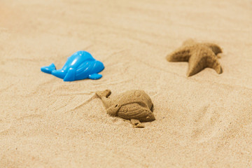 Fototapeta na wymiar toys, childhood and vacation concept - sand shape made by whale mold on summer beach
