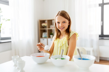 easter, holidays and people concept - happy girl coloring eggs by liquid dye at home
