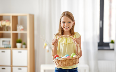 easter, holidays and people concept - happy girl with basket of colored eggs at home