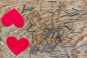 two red hearts on wooden background surrounded by iron nails