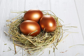 Golden eggs in a basket with hay on a white wooden . Easter composition.