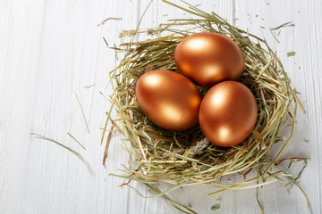 Golden eggs in a basket with hay on a white wooden . Easter composition.