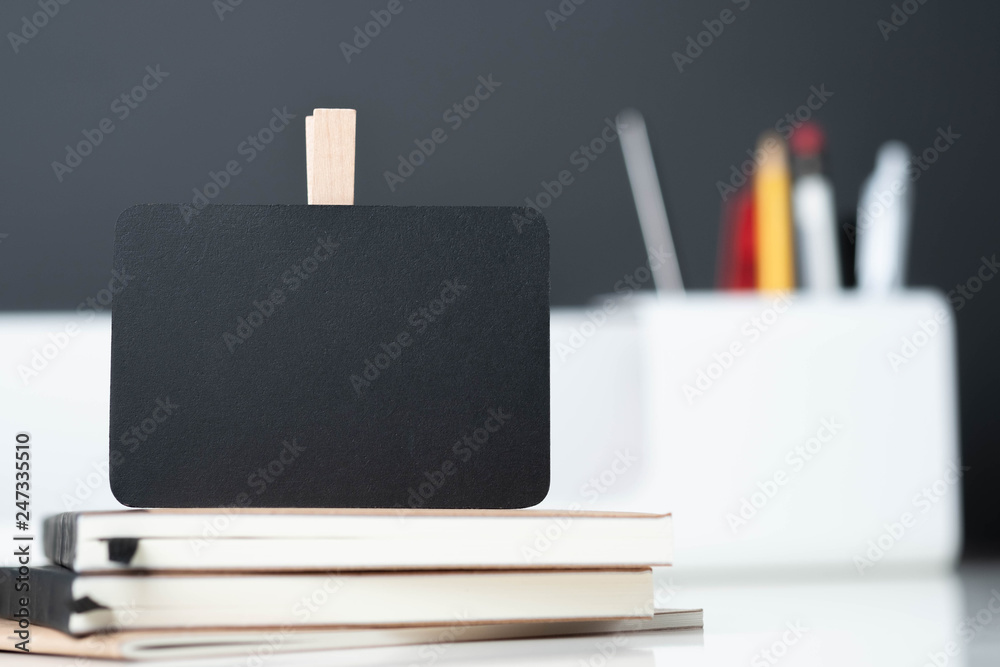 Poster close up clip blackboard on notebook with blur modern pencil box  on table and dark grey wall in office desk,mock up space for display of design or text.