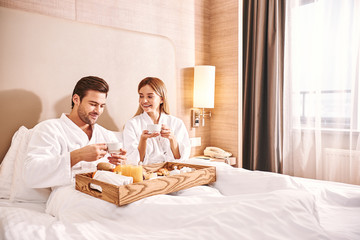 Food delivery in the room. Couple are eating in hotel room bed
