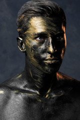 a man in black make-up with gold. portrait of a guy in dark paint with gold. Artistic portrait photography