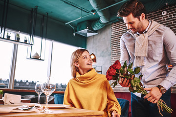 Red roses for woman. Man in blue shirt surprised his pretty blonde girlfriend