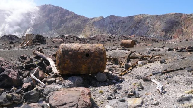 Handheld shot of corroded metal barrels at abandoned sulphur mine on White Island in New Zealand. Steam emitting from fumarole in ground