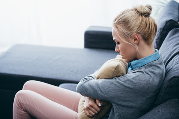 Obraz premium depressed woman sitting on couch and holding pillow at home