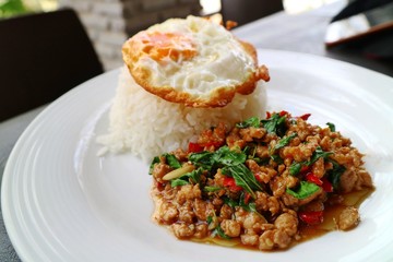 Rice with spicy fried pork with basil leaves and fried egg on white plate. Thai style food. Food concept.  