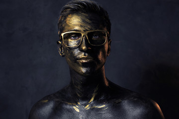a man in black make-up with gold. portrait of a guy in dark paint with gold. Artistic portrait...